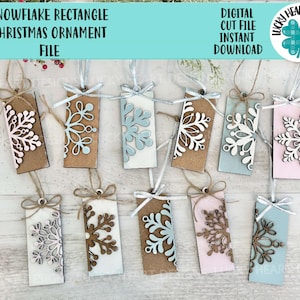 May include: Twelve rectangle-shaped Christmas ornaments with a snowflake design. The ornaments are painted in various colors, including brown, pink, blue, and white. The snowflakes are cut out of the ornaments, creating a layered effect. The ornaments are strung with twine and ready to be hung on a Christmas tree.