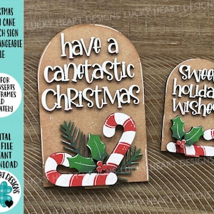 May include: Two Christmas-themed wooden signs. One sign says "Have a canetastic Christmas" with a candy cane and holly. The other says "Sweet Holiday Wishes" with a candy cane and holly. The signs are brown with white lettering.