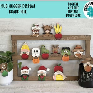 May include: A wooden display board with various themed mug huggers. The mug huggers include a gingerbread man, Santa, gnomes, and Halloween characters. The text "Mug Hugger Display Board File" is at the top.