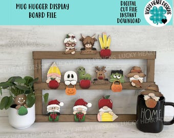 May include: A wooden display board with various themed mug huggers. The mug huggers include a gingerbread man, Santa, gnomes, and Halloween characters. The text "Mug Hugger Display Board File" is at the top.