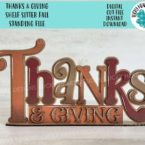 May include: A wooden shelf sitter sign with the words "Thanks & Giving" in a fall-themed color scheme. The sign is designed for a standing display and is perfect for fall decor.