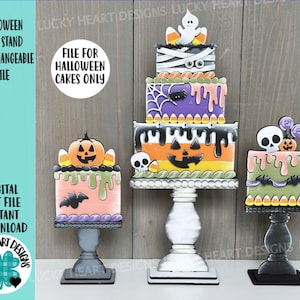 May include: Three Halloween-themed cake stands with interchangeable designs. Each stand features a square cake with spooky decorations like pumpkins, ghosts, and spiders. The cakes are in various colors, including orange, purple, and green, and are displayed on decorative pedestals.