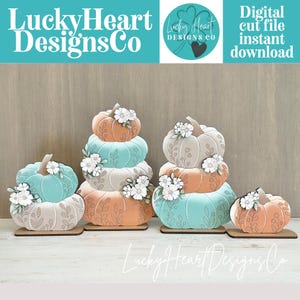 May include: A set of four decorative wooden pumpkin stacks in shades of teal, peach, and cream. Each pumpkin features etched floral and vine patterns and is accented with white flower cutouts. The pumpkins are mounted on flat wooden bases.