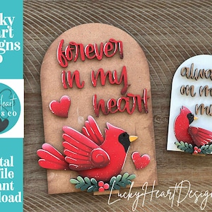 以下が含まれることがあります： カーディナルバードのデザインが施された木製の切り抜き装飾。1つは「forever in my heart」、もう1つは「always on my mind」と書かれています。どちらも赤いカーディナルとハートのアクセントがあります。「Lucky Heart Designs Co」の文字も表示されています。