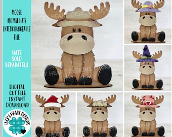 May include: A set of five digital cut files for a moose with interchangeable hats. The hats include a ranger hat, a purple flower hat, a witch hat, a flower crown, and a pink heart hat. The moose is brown with black hooves and a white nose. The hats are all different colours and designs. The text "MOOSE ANIMAL HATS INTERCHANGEABLE FILE" is in the top left corner of the image. The text "HATS SOLD SEPARATELY" is in the middle left corner of the image. The text "DIGITAL CUT FILE INSTANT DOWNLOAD" is in the bottom left corner of the image. The text "LUCKY HEART DESIGNS" is in a green circle with a clover in the bottom left corner of the image.