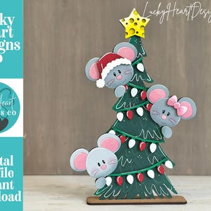 May include: A decorative wooden cutout featuring a green Christmas tree adorned with red and white light bulbs and a yellow star topper. Three grey mice with pink ears are positioned around the tree, one wearing a red Santa hat and one with a pink bow.