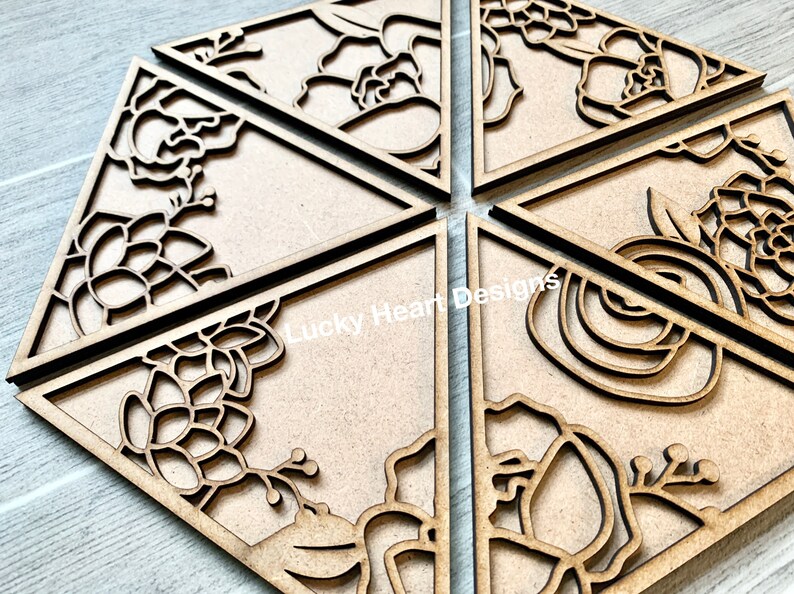 May include: Six wooden triangle-shaped signs with intricate floral designs cut out. The designs include flowers, leaves, and vines. The signs are unfinished and ready to be painted or stained.
