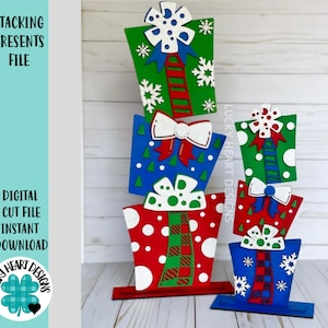 May include: A stack of four wooden Christmas presents painted in red, green, blue, and white with polka dots, snowflakes, and plaid patterns. The presents are stacked on a wooden base.