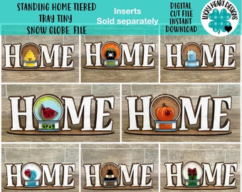 May include: Six different snow globe designs with the word "HOME" in white letters on a wooden base. The snow globes feature various themes, including a beehive, a spider, a watermelon, a pumpkin, a balloon, and a present.