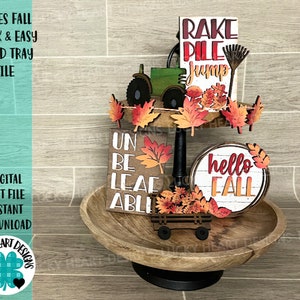 Puede incluir: Una bandeja de niveles decorada para el otoño con un letrero de madera que dice "hello fall", un letrero de madera que dice "rake pile jump", un letrero de madera que dice "un be leaf able", un pequeño tractor de juguete y hojas de otoño.