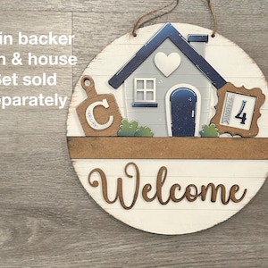Puede incluir: Un letrero de bienvenida redondo de madera con un dise&ntilde;o de casa y tabla de cortar. El letrero presenta una casa con un coraz&oacute;n, una tabla de cortar con la letra "C" y las palabras "Party of 4". La palabra "Welcome" est&aacute; escrita en cursiva.