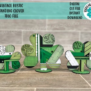 May include: Three standing wooden clover cutouts with a vintage rustic design. The clovers are painted in shades of green, black, and white with a patchwork pattern. The clovers are on a wooden base.
