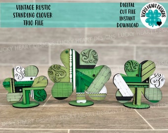 May include: Three standing wooden clover cutouts with a vintage rustic design. The clovers are painted in shades of green, black, and white with a patchwork pattern. The clovers are on a wooden base.