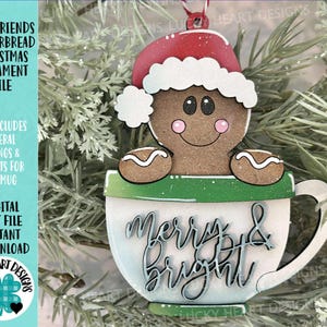 Puede incluir: Adorno navideño de madera con un hombre de jengibre con un gorro de Papá Noel, saliendo de una taza. La taza es blanca con un borde verde y las palabras "Merry & Bright". Es un archivo de corte digital.