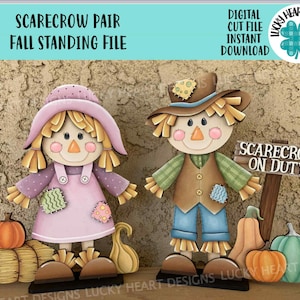 May include: Two wooden scarecrow figures, one female and one male, with fall-themed decorations. The female scarecrow wears a pink dress and hat. The male scarecrow has a brown hat and vest. Pumpkins and a sign that says "SCARECROW ON DUTY" are also present.
