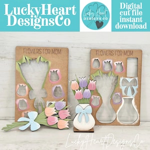 May include: Wooden cut file designs with the text "FLOWERS FOR MOM". One design features a bouquet of tulips with a blue bow, and the other has a vase with tulips and a bow. The image also includes the text "Lucky Heart Designs Co" and "Digital cut file instant download".