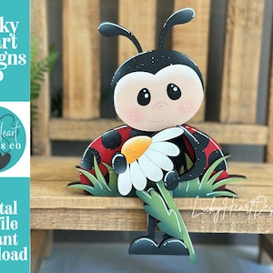 May include: A wooden ladybug decoration with a smiling face, holding a daisy. The ladybug has a red and black shell, with green grass and leaves at the base. The text "Lucky Heart Designs Co" and "Digital cut file instant download" are visible.