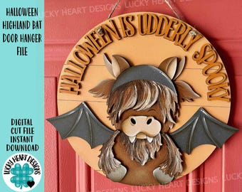 May include: A round wooden Halloween door hanger featuring a Highland cow with bat wings. The text "HALLOWEEN IS UDDERLY SPOOKY" is displayed around the cow. The sign is light brown with dark brown and gray accents.