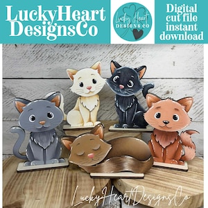 May include: A collection of five wooden cat figurines in various colors, including gray, white, black, and orange. One cat is curled up asleep. The image includes the text "Lucky Heart Designs Co" and "Digital cut file instant download."
