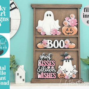 May include: A brown wooden tiered shelf display featuring layered Halloween-themed cutouts. The top shelf holds a white ghost and pink flowers with a pumpkin. The middle shelf displays the word BOO with pumpkins. The bottom shelf features the text ghost KISSES & flower WISHES next to a ghost wearing a witch hat.