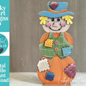 May include: A decorative wooden scarecrow figure composed of three stacked orange pumpkins. The scarecrow wears a blue hat with a patch, yellow straw hair, and a green plaid vest with orange buttons. Various colorful patches adorn the pumpkins.