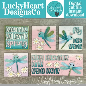 May include: A selection of wooden signs with dragonfly and floral motifs. The signs display phrases such as "Dragonflies Welcome Spring" and "Fly Into Spring." The colour scheme includes teal, pink, and white, with the text "Lucky Heart Designs Co."
