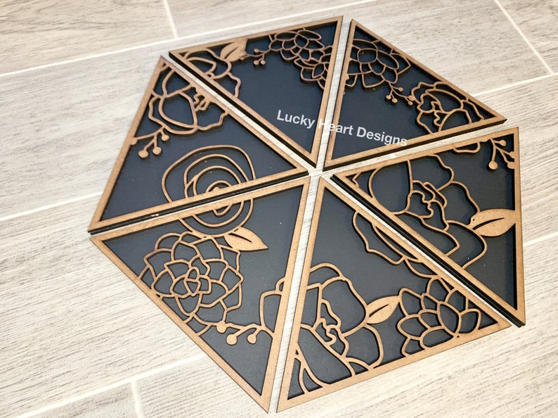 May include: Six black and brown wooden triangular wall decor pieces with floral designs. The pieces are arranged in a hexagonal shape. The text "Lucky Heart Designs" is visible on one of the pieces.