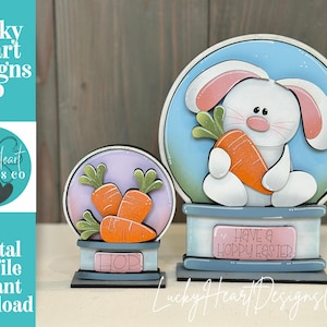 May include: Two Easter-themed wooden decorations. One features a white bunny holding an orange carrot, set against a blue backdrop. The other has three orange carrots. Both have a base with text. The text "Have a Hoppy Easter" is visible.