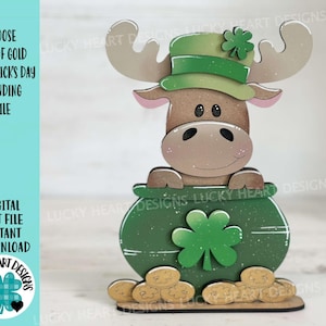 May include: A wooden moose figure with a green hat and a pot of gold, designed for St. Patrick's Day. The moose is brown with a light pink nose and ears. The pot is green with a shamrock and gold coins at the base. Text on the left says "MOOSE POT OF GOLD ST. PATRICK'S DAY STANDING FILE".