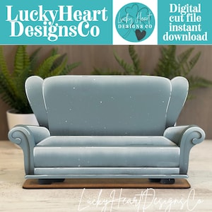 May include: A light blue, two-seater sofa cutout with a high back, curved armrests, and a flat base. The design features a smooth, matte finish with subtle white highlights along the edges, resting on a thin, rectangular brown wooden platform.