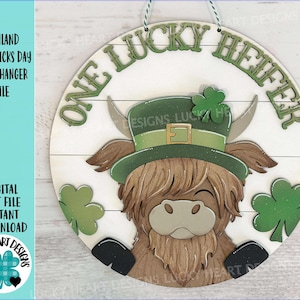 May include: Wooden round door hanger featuring a Highland cow wearing a green leprechaun hat and shamrocks. The text "ONE LUCKY HEIFER" is arched across the top. The words "HIGHLAND ST PATRICKS DAY DOOR HANGER FILE" are on the left side.