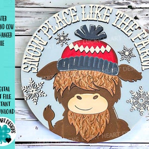 Puede incluir: Un letrero redondo de madera con fondo azul y el texto "Snow Place Like The Farm". Una vaca Highland de dibujos animados con un gorro de invierno rojo y azul está en el centro del letrero.