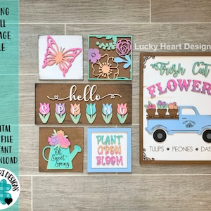 Puede incluir: Un collage de pared con temática primaveral que presenta cinco letreros de madera con diseños recortados. Los letreros incluyen una mariposa, un diseño floral, un letrero que dice "hello spring" con tulipes, una regadera con flores y el texto "Oh Sweet Spring", y un letrero que dice "Plant Grow Bloom". Los letreros están dispuestos sobre un fondo de madera. El texto "Lucky Heart Designs" es visible en la esquina superior derecha.