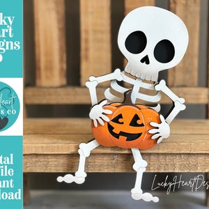 May include: A white skeleton figure with black eye sockets and a nose cavity, holding an orange jack-o'-lantern pumpkin with a black carved face. The text Lucky Heart Designs Co Digital cut file instant download is visible on the left side.
