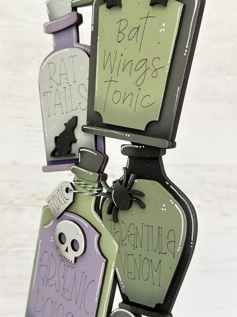 May include: Wooden Halloween potion bottles with labels reading "Rat Tails," "Bat Wings Tonic," "Arsenic Poison," and "Tarantula Venom." The bottles are in shades of purple, green, and black, with a rat, skull, and spider embellishments.
