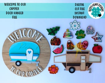 May include: A wooden door hanger with a welcome to our camper sign. The sign features a blue camper with a white roof and a heart on the back. The sign is surrounded by various wooden cutouts, including a watermelon, a pumpkin, a heart, a snowflake, a tree, a star, and a lucky clover.