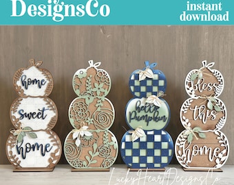 May include: Four stacked pumpkin-shaped wooden signs with laser-cut designs. The first features 'home sweet home' text, the second has floral patterns, the third displays 'hello pumpkin' with a blue plaid, and the fourth reads 'Bless this home'.