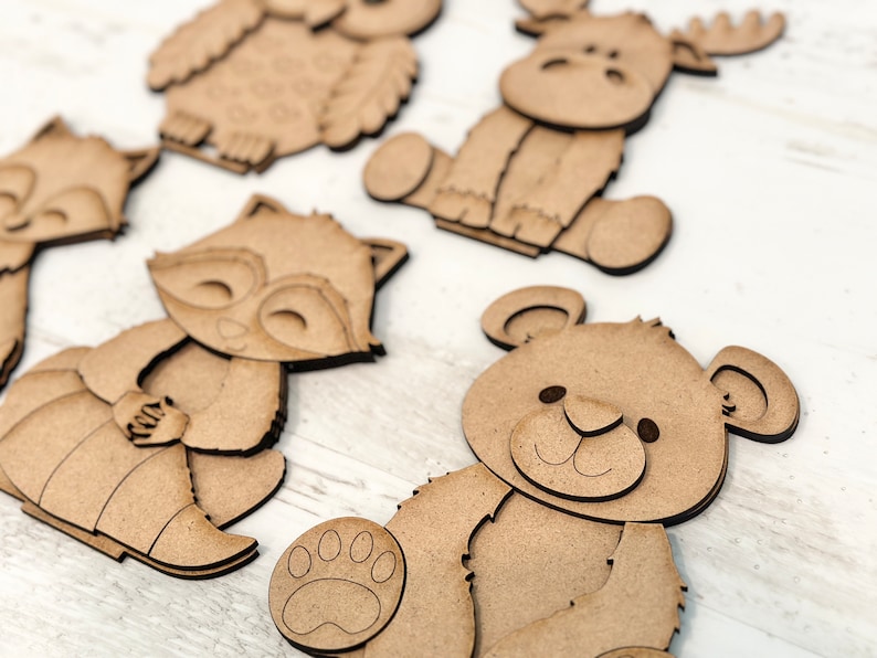 Pu&ograve; includere: Cinque sagome di animali in legno, tra cui un gufo, un alce, un procione, una volpe e un orso. Le sagome sono tutte marroni e hanno caratteristiche semplici e cartoon.