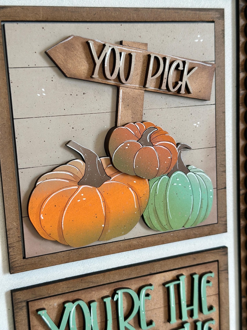 Peut inclure: Panneau en bois avec les mots "YOU PICK" au-dessus de trois citrouilles dans des tons orange et vert. Les citrouilles sont plac&eacute;es sur un fond brun clair avec un cadre en bois. Le panneau est une d&eacute;coration sur le th&egrave;me de l'automne.