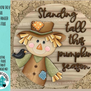 Peut inclure: Panneau de porte rond en bois avec un épouvantail et un corbeau. L'épouvantail porte un chapeau de paille, des joues roses et un patch cousu. Le texte dit "Standing tall this pumpkin season."