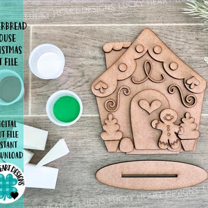 Könnte beinhalten: Ein Weihnachts-Bastelset für ein Lebkuchenhaus mit einem Lebkuchenmann und einem Herz-Design. Das Set enthält ein Lebkuchenhaus aus Holz, einen Lebkuchenmann und eine herzförmige Aussparung. Das Set ist zum Bemalen und Dekorieren gedacht.