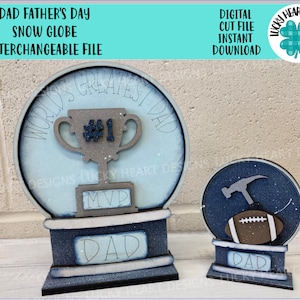 May include: Two snow globes with a Father's Day theme. One features a trophy with "WORLD'S GREATEST DAD" and "MVP" text. The other has a football and hammer. Both have "DAD" on the base. The text "DAD FATHER'S DAY SNOW GLOBE INTERCHANGEABLE FILE" is at the top.