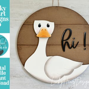 Könnte beinhalten: Runder Holzschild mit einer weißen Gans mit orangefarbenem Schnabel und schwarzen Augen. Die Gans ist vor einem braunen Hintergrund mit dem Wort "hi!" in Schwarz platziert. Das Schild ist eine digitale Schnittdatei.