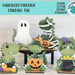 May include: A collection of Halloween-themed dinosaur cutouts. The dinosaurs are green and decorated as a ghost, mummy, and witch. One dinosaur holds a jack-o'-lantern. The text "HALLOWEEN DINOSAUR STANDING FILE" is at the top. The words "DIGITAL CUT FILE INSTANT DOWNLOAD" are also visible.