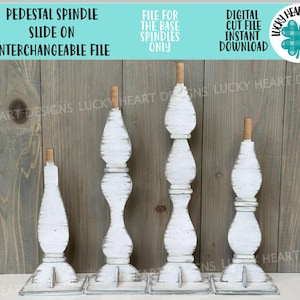 Może przedstawiać: Cztery białe, postarzane wrzeciona cokołowe z drewnianym kołkiem na górze. Wrzeciona mają różne wysokości i dekoracyjny, toczony wzór. Tekst na górze brzmi "PEDESTAL SPINDLE SLIDE ON INTERCHANGEABLE FILE".