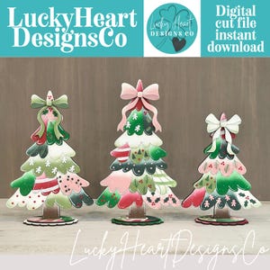 May include: Three decorative Christmas tree cutouts featuring scalloped layers in shades of green, red, pink, and white with gingerbread man and holly patterns. Each tree is topped with a large bow and stands on a circular base.
