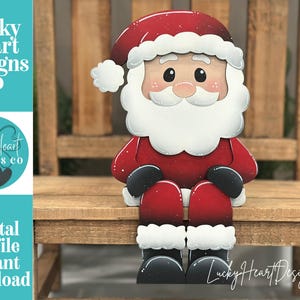 May include: A wooden Santa Claus figure with a red suit, hat, and boots, and a white beard and trim. The figure is sitting on a small wooden bench. The text "Lucky Heart Designs Co" and "Digital cut file instant download" are visible.