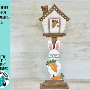 Peut inclure: Un lapin blanc portant des lunettes bleues tenant une carotte se tient devant un nichoir en bois avec une porte rose. Le nichoir est sur un support en bois. Le lapin et le nichoir sont tous deux découpés dans du bois et prêts à être assemblés.