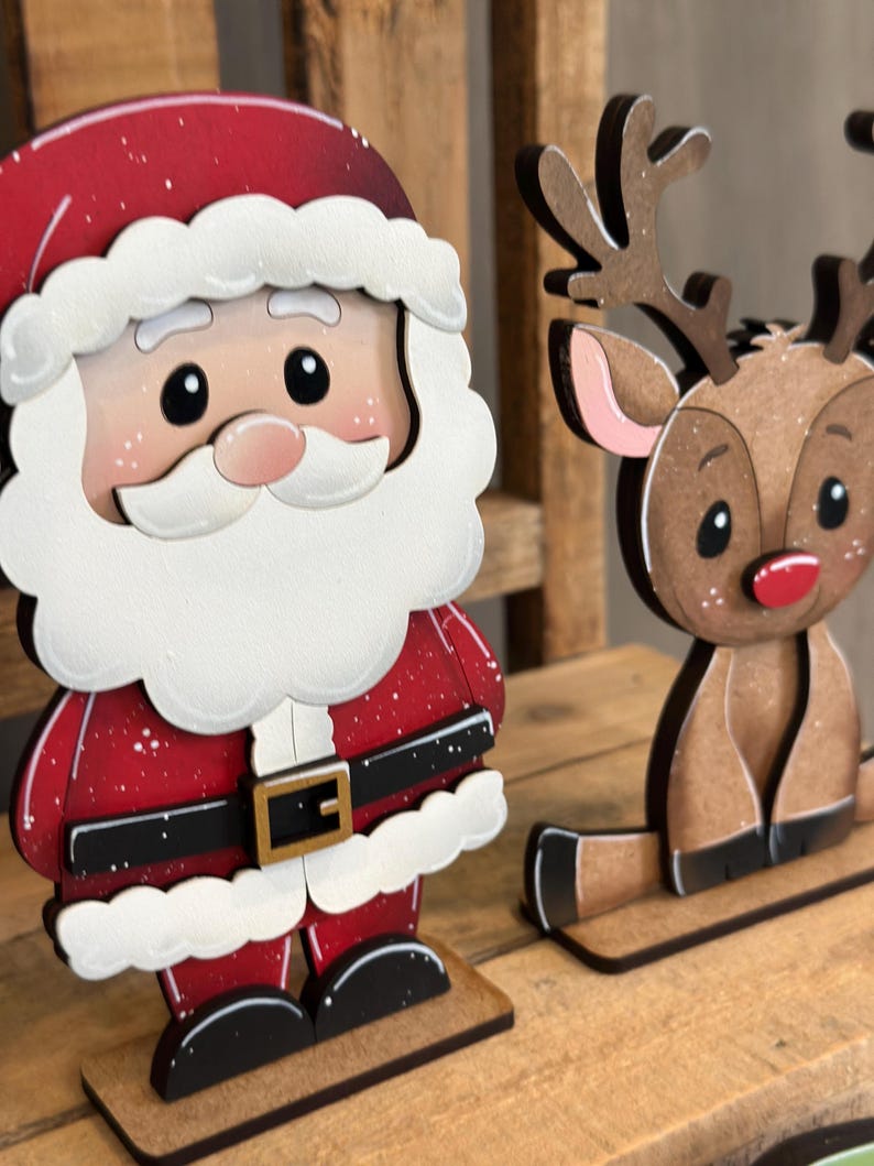 May include: Wooden Christmas decorations featuring Santa Claus and a reindeer. Santa is in a red suit with white trim and a black belt. The reindeer is brown with antlers and a red nose. Both are on wooden bases.