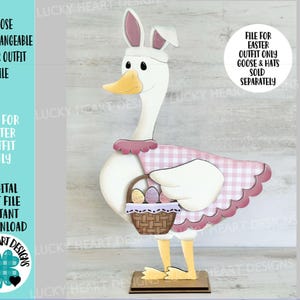 Könnte beinhalten: Eine Holzfigur einer Gans mit rosa Vichy-Outfit und Hasenohren, die einen Korb mit Ostereiern trägt. Die Gans steht auf einem Holzsockel. Der Text lautet: "Goose Interchangeable Easter Outfit File".